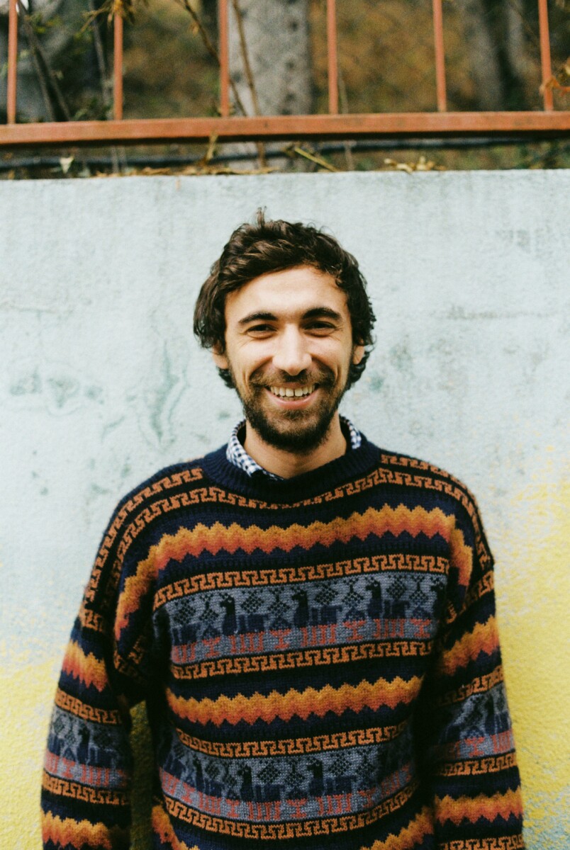 Cheerful man in multicolored sweater standing near concrete wall outdoors